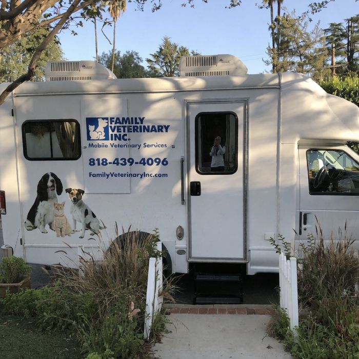 Mobile veterinary van parked outside, featuring images of a dog, cat, and rabbit with contact information and company logo.